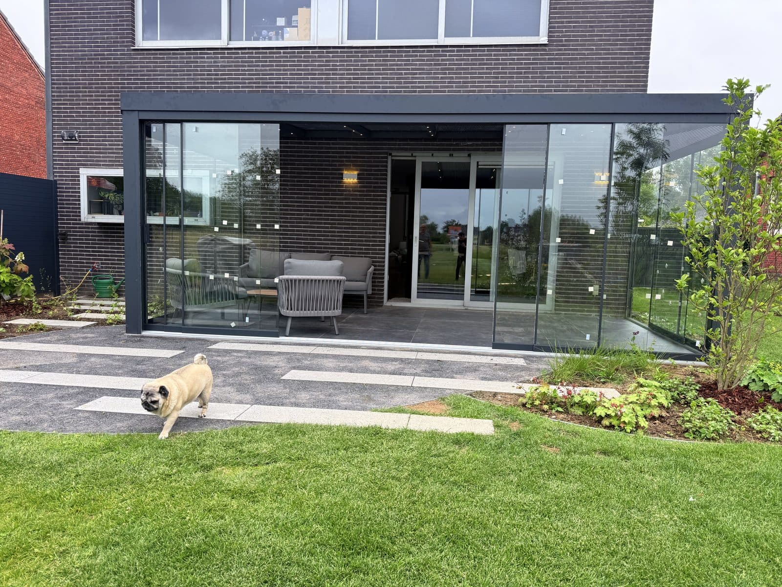 Terrasoverkapping met glazen schuifwanden aan een moderne nieuwbouwwoning, gezien vanaf het gazon