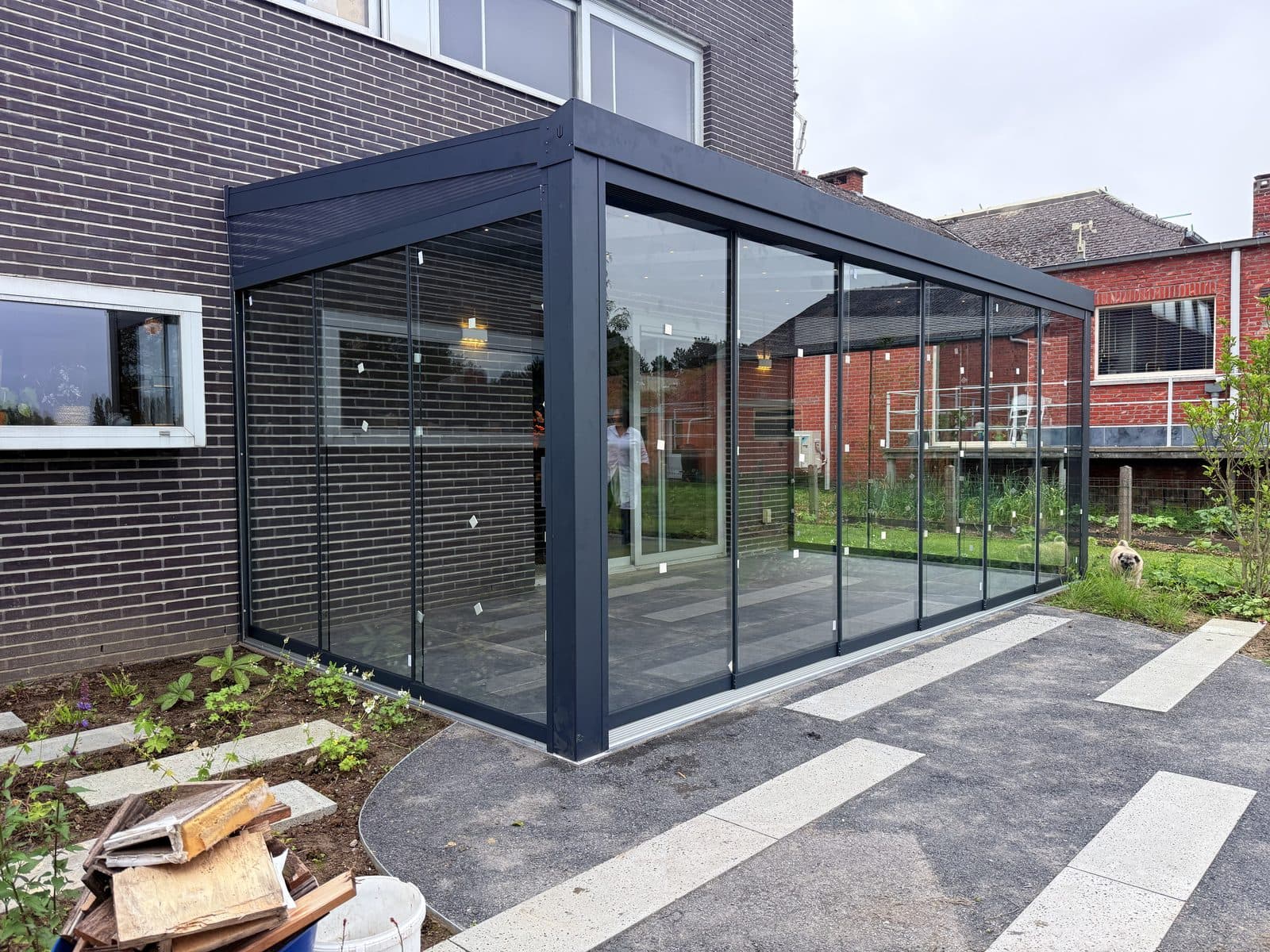 Zijaanzicht van de overkapping met glazen schuifwanden en antracieten profielen