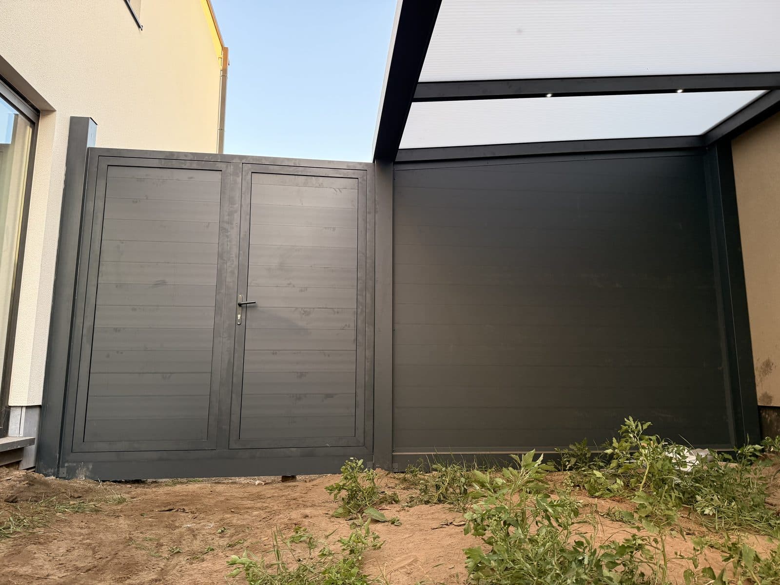 De bergingswand met dubbele deur naast de carport