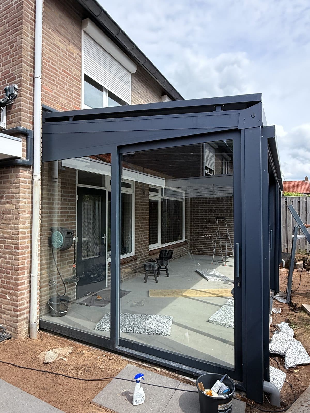 Antraciet overkapping met glazen wanden en schuifpui tegen de achtergevel